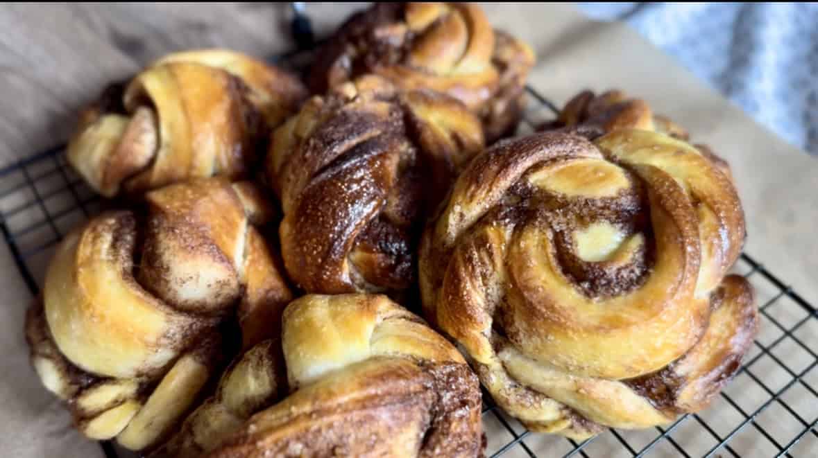 Close-up of several cinnamon buns with a golden-brown crust, cooling on a black wire rack.