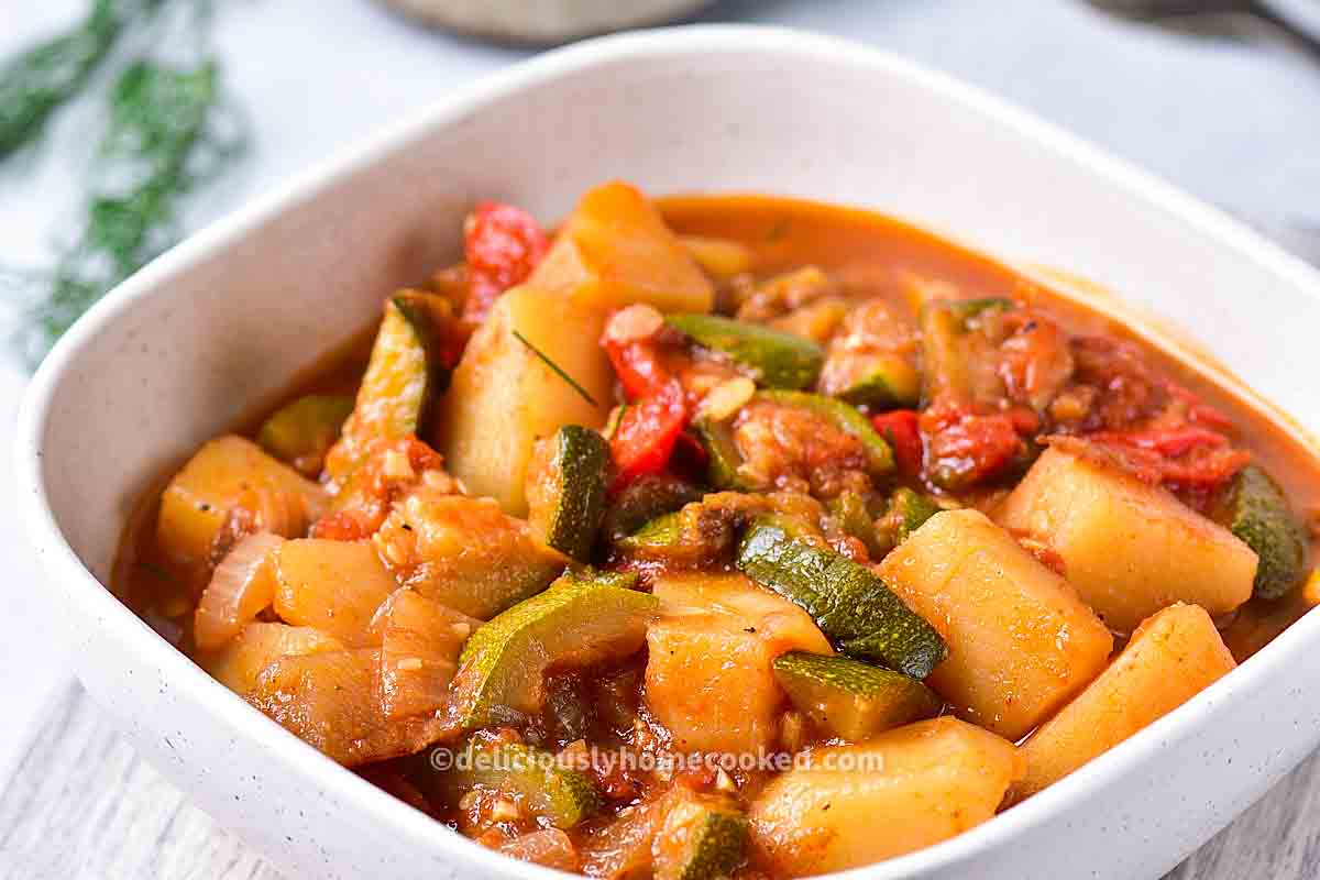 A bowl of vegetable stew with potatoes, zucchini, tomatoes, and onions in a tomato-based sauce.