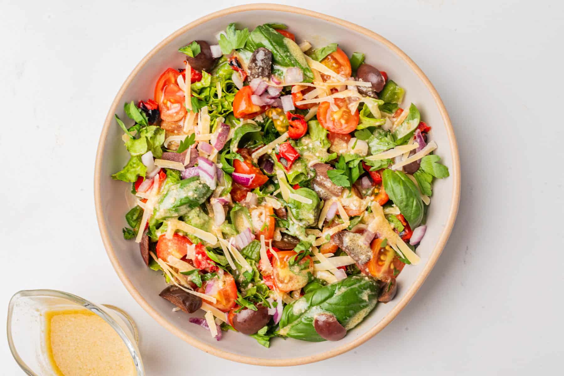 A bowl of mixed salad with lettuce, cherry tomatoes, olives, shredded cheese, red onion, and dressing, viewed from above.