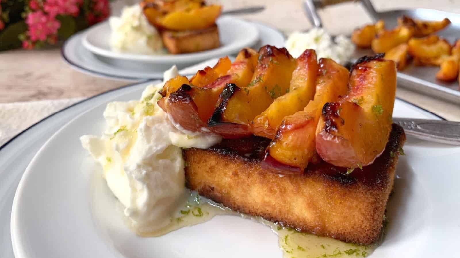 A slice of toasted pound cake topped with grilled peaches and served with a dollop of whipped cream on a white plate.