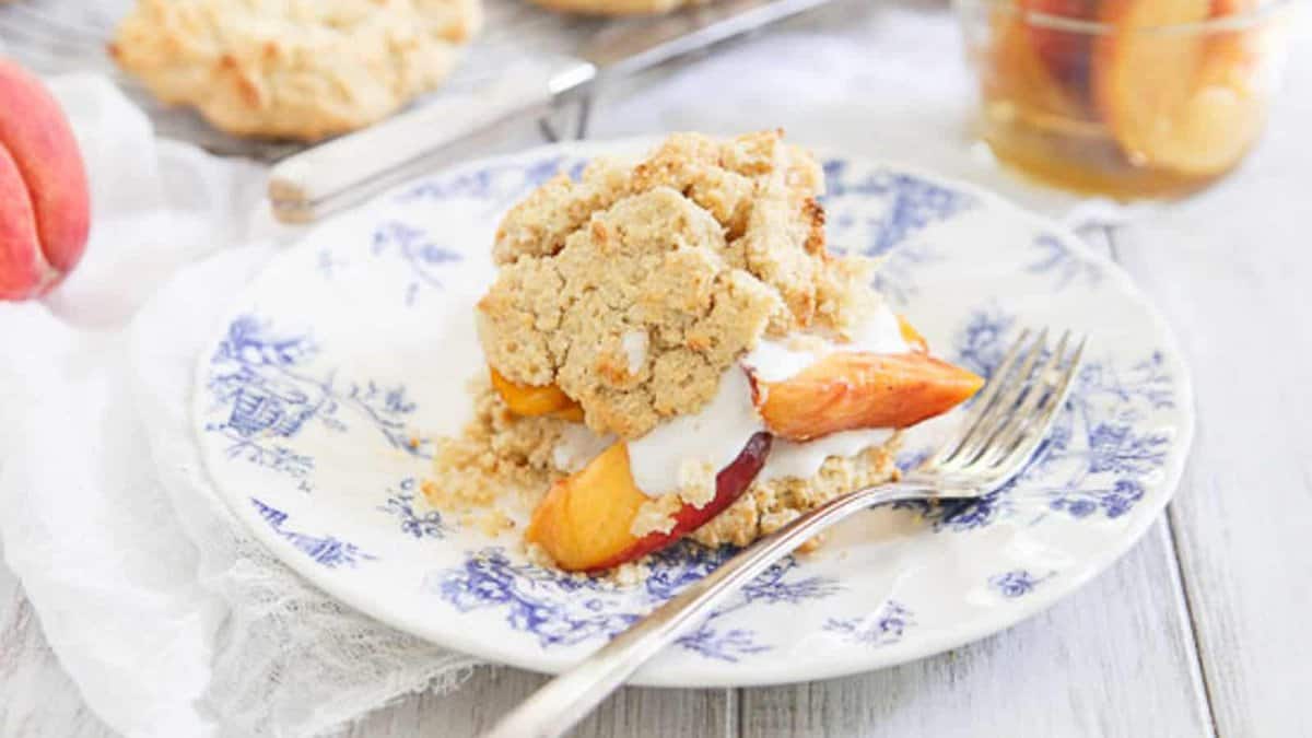 A peach shortcake dessert with cream and peach slices on a blue and white plate, with a fork beside it.