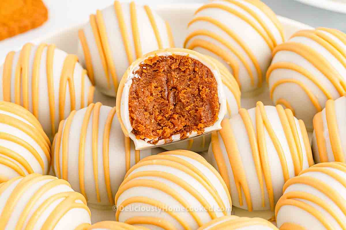 A plate of white chocolate-coated truffles with orange drizzle; one truffle cut in half reveals a crumbly brown filling.