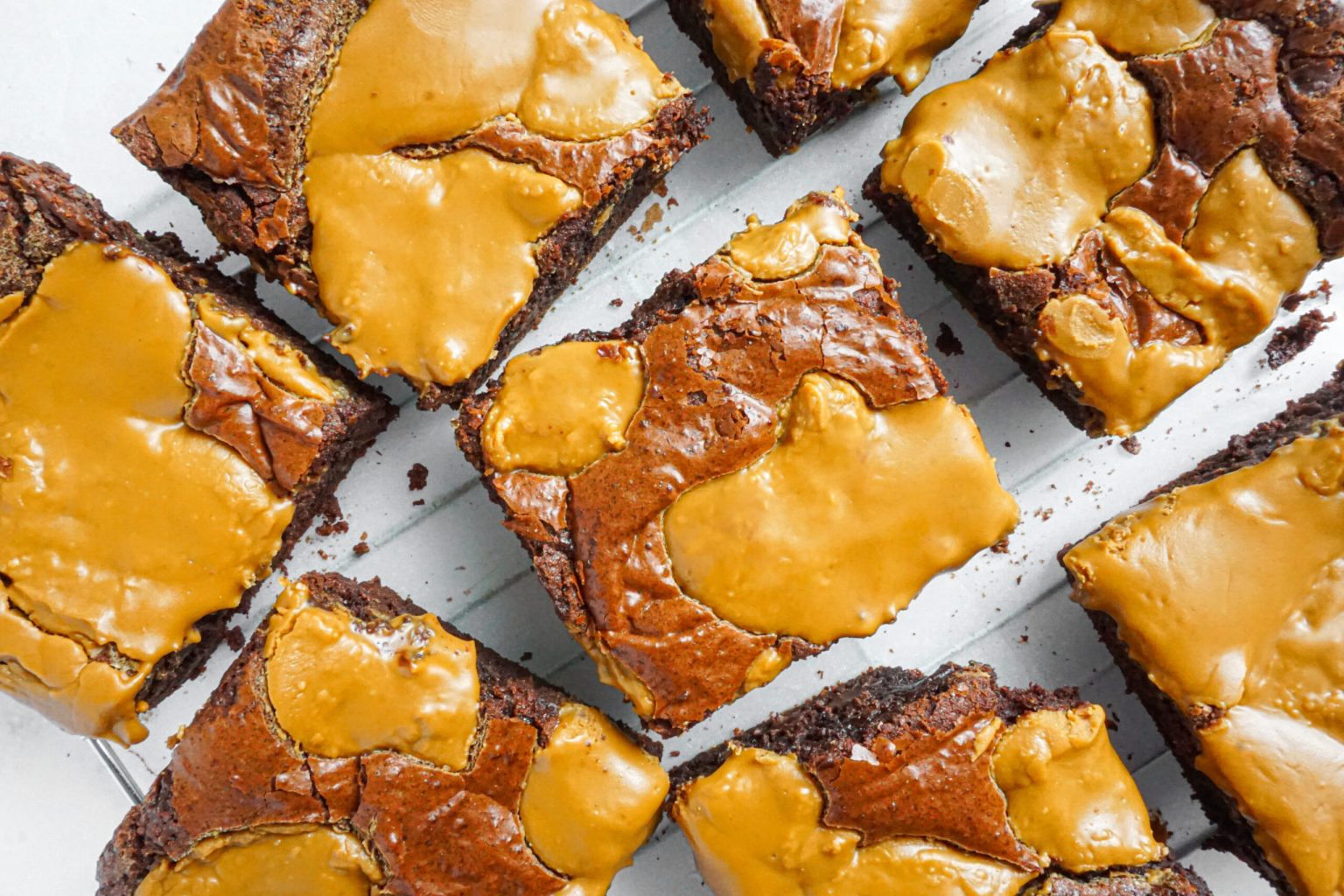 Several square brownies topped with a layer of melted caramel are arranged on a white surface.