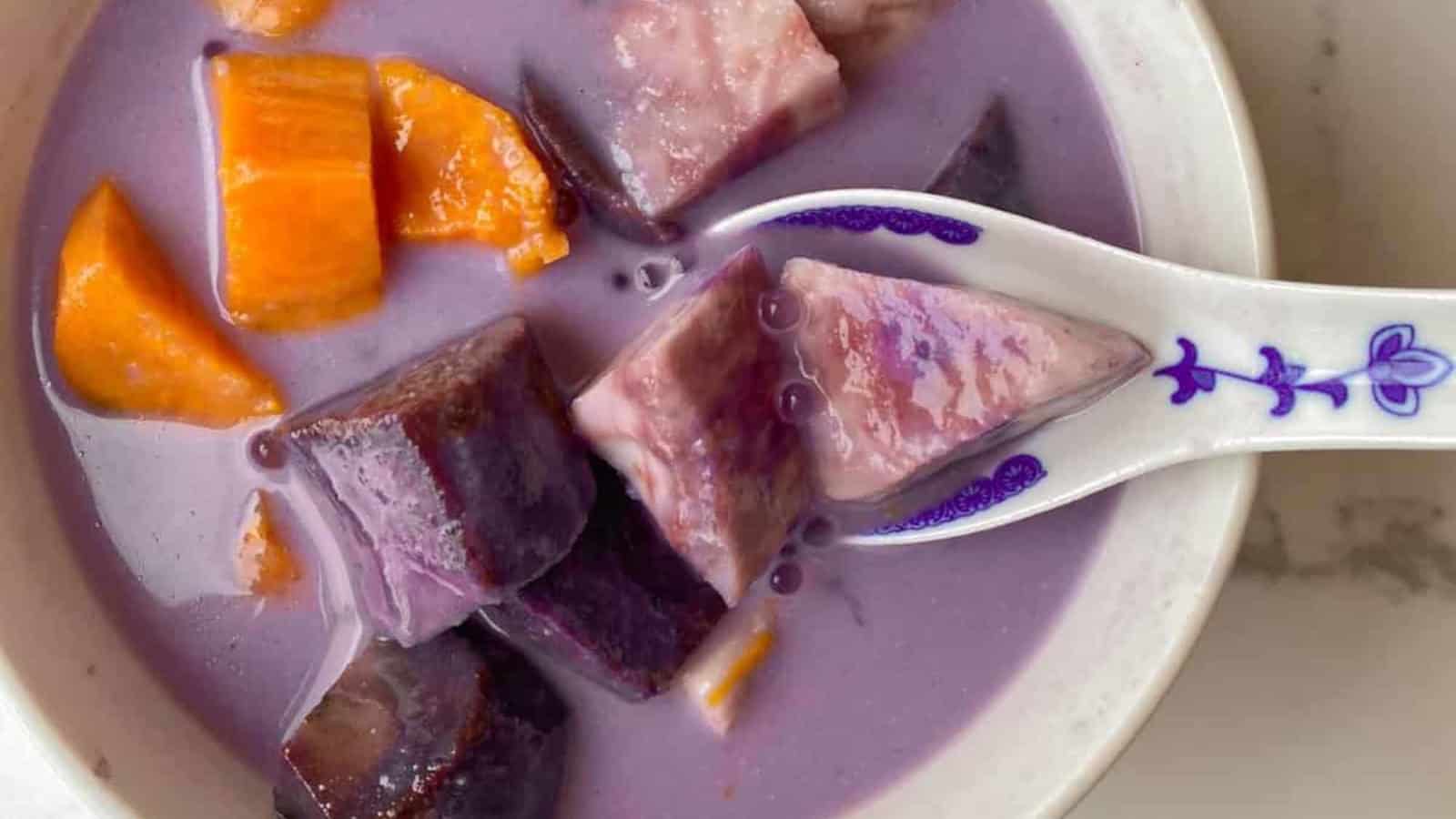 A bowl of purple sweet potato dessert soup with orange and purple yam cubes, served with a porcelain spoon.