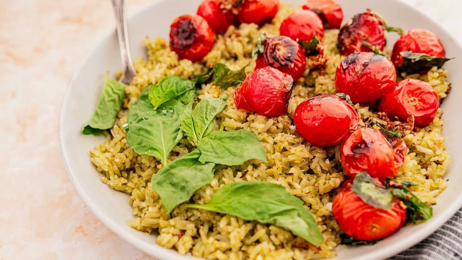 A plate of pesto rice topped with roasted cherry tomatoes and fresh basil leaves.
