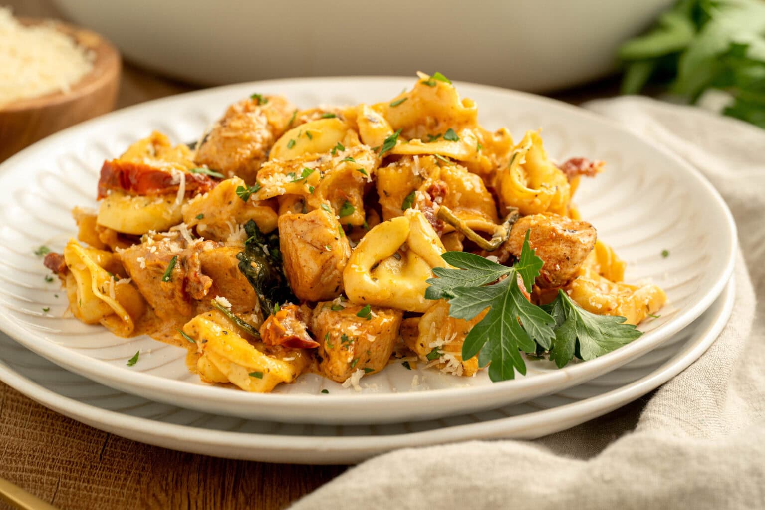 A plate of tortellini pasta with pieces of chicken, sun-dried tomatoes, spinach, and parsley garnish, served on a white dish.