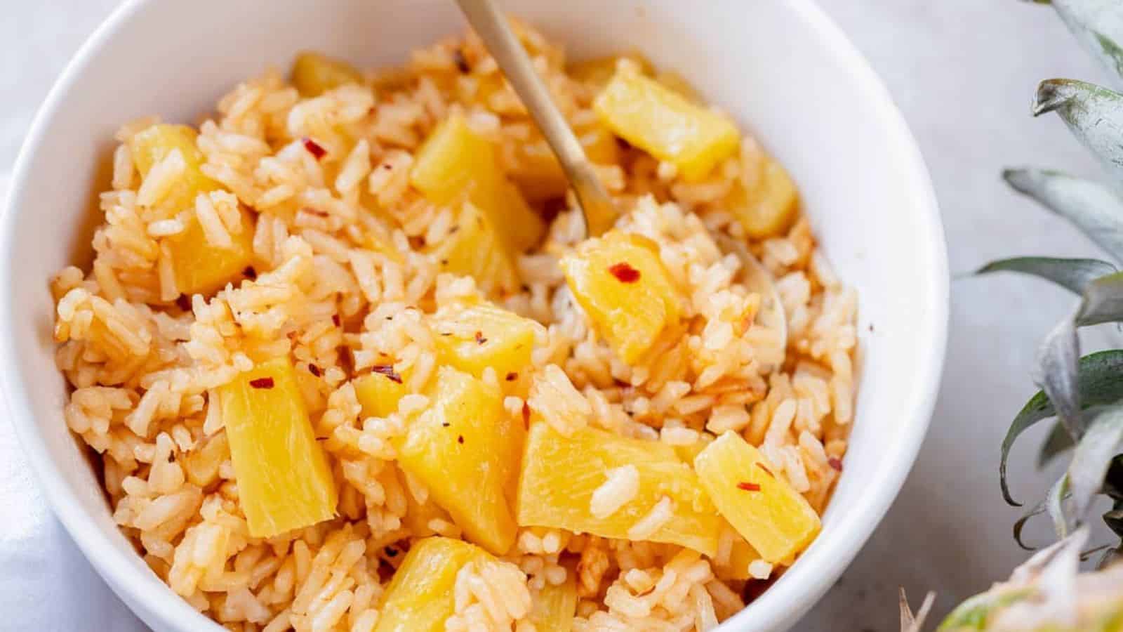 A white bowl filled with cooked rice and pineapple chunks, with a spoon resting inside.