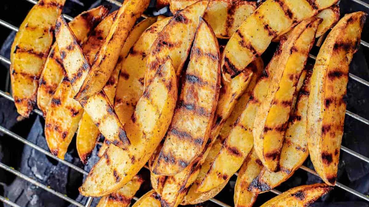 Grilled potato wedges with visible char marks arranged on a metal grill over hot coals.