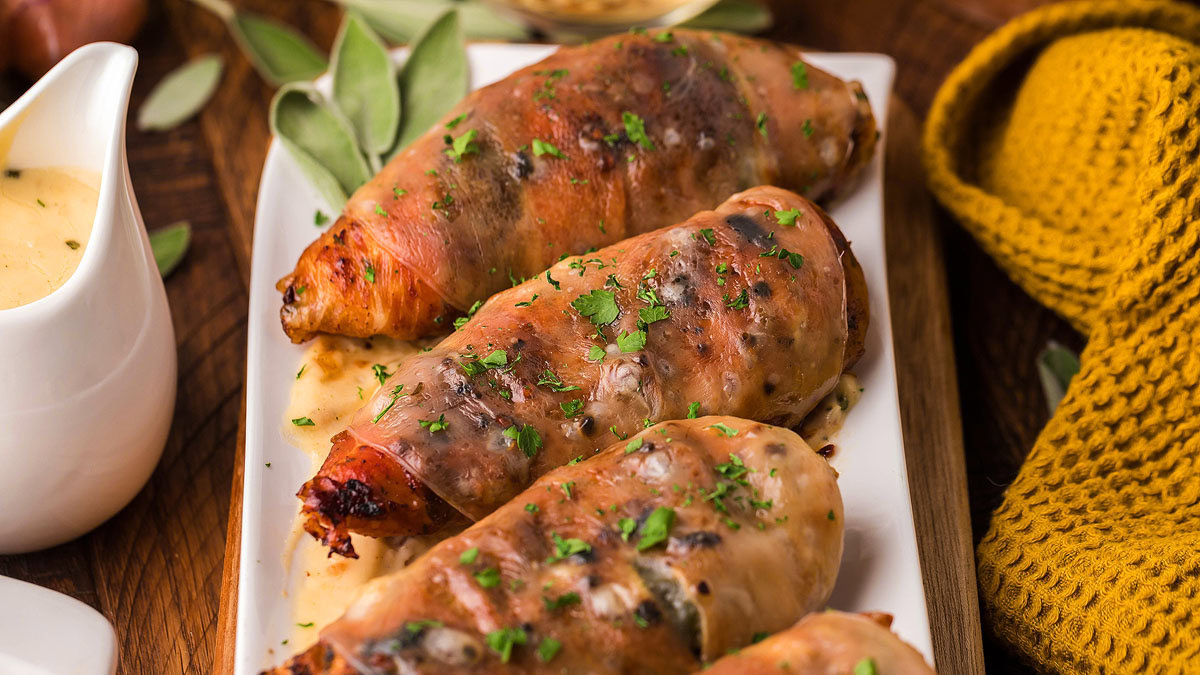 Three pieces of stuffed, browned chicken breasts garnished with chopped herbs on a rectangular white plate, with a yellow knit cloth and a small pitcher of sauce nearby.