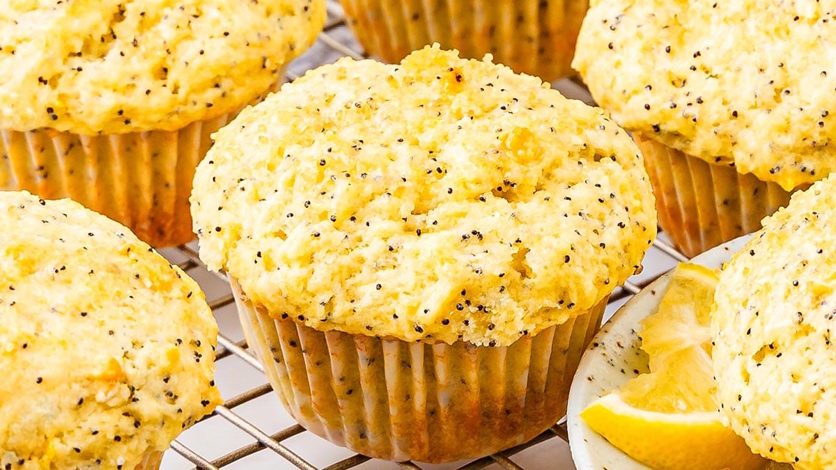 Lemon poppy seed muffins rest on a cooling rack with a lemon wedge nearby.