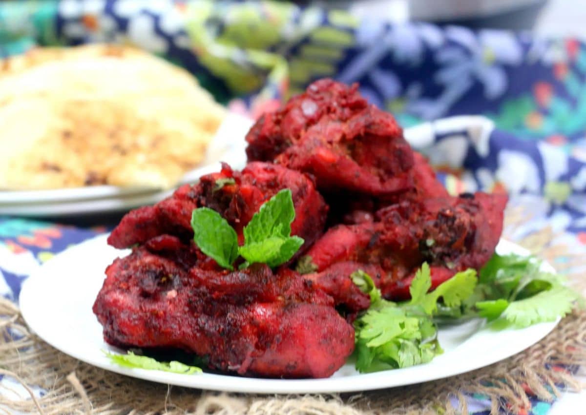 A plate of red, fried chicken pieces garnished with fresh mint and cilantro, with a side of bread in the background.