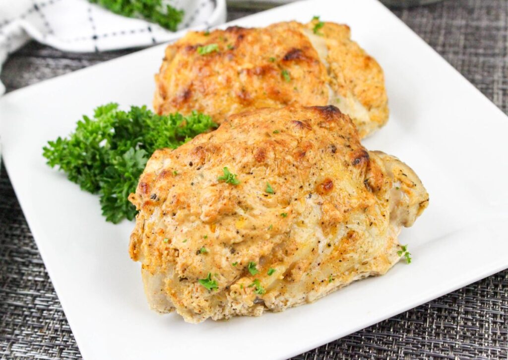 Two pieces of seasoned, baked chicken on a white plate, garnished with fresh parsley.