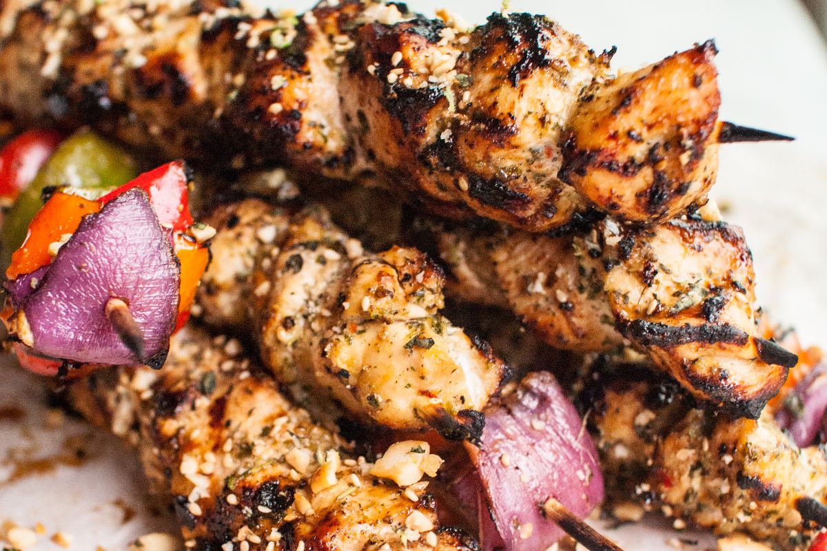 Close-up of grilled chicken skewers with pieces of red onion and bell pepper, seasoned with herbs and spices.