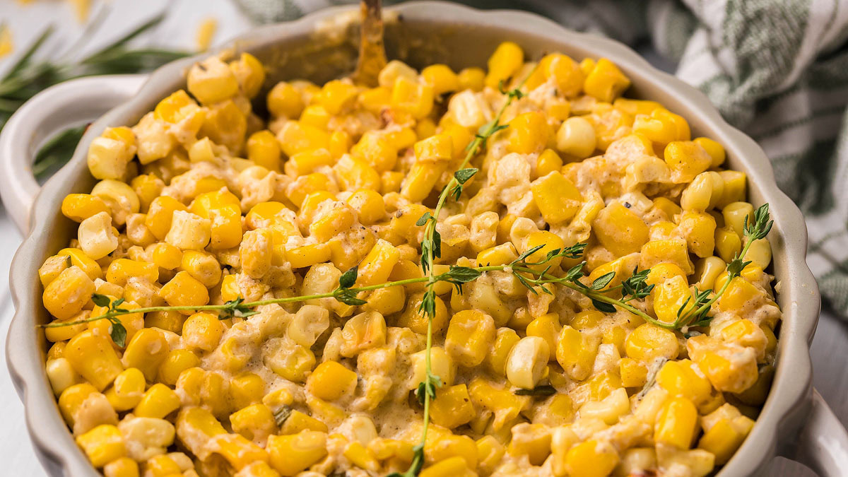 A casserole dish filled with creamy baked corn, garnished with sprigs of fresh thyme.