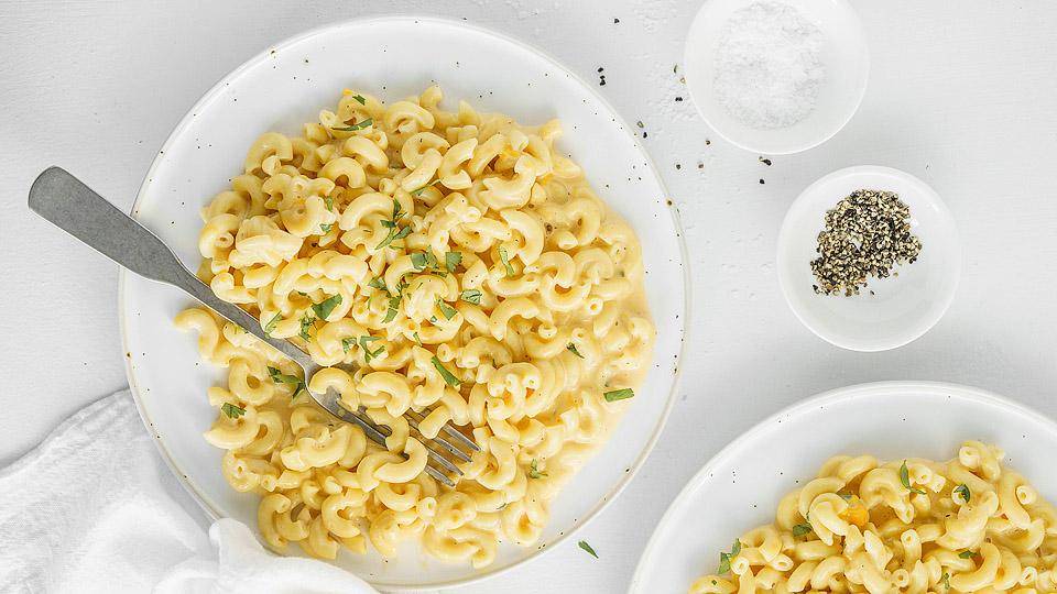 A plate of macaroni and cheese garnished with herbs, next to small bowls of salt and pepper on a white table.
