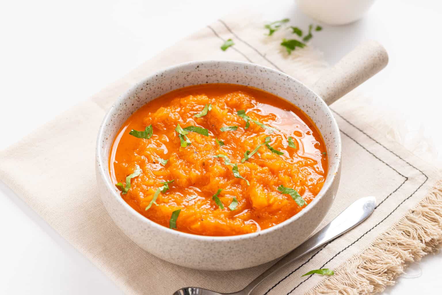 A bowl of orange-colored tomato and egg stir-fry garnished with chopped herbs, placed on a beige napkin with a spoon beside it.