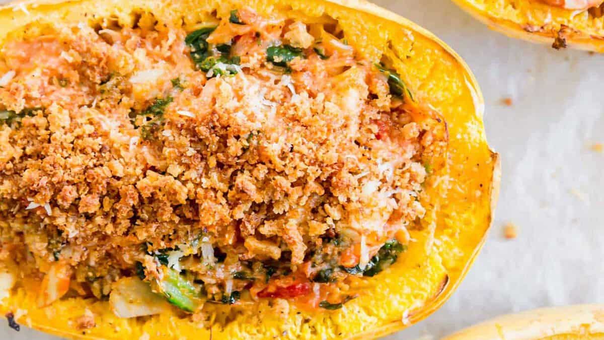 A close-up of a baked spaghetti squash half filled with a vegetable mixture and topped with a golden breadcrumb crust.