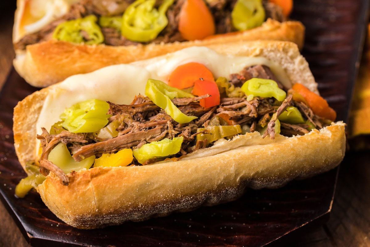 A sandwich with shredded beef, melted cheese, sliced carrots, and pepperoncini served in a hoagie roll.