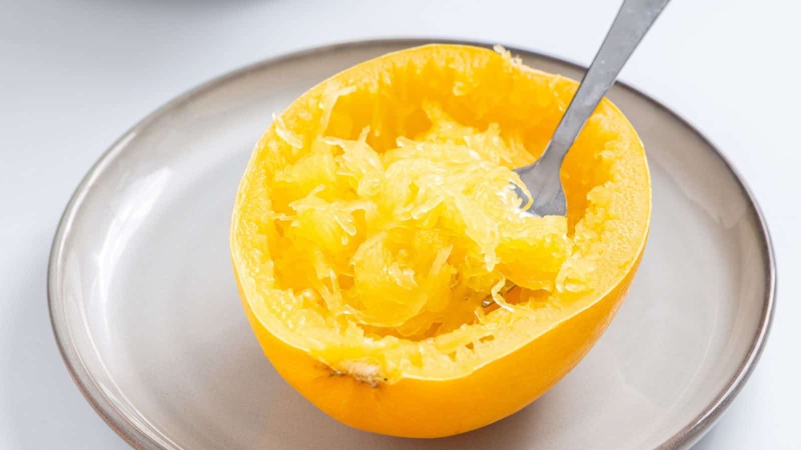 A halved spaghetti squash on a plate with a fork scraping out the stringy flesh.