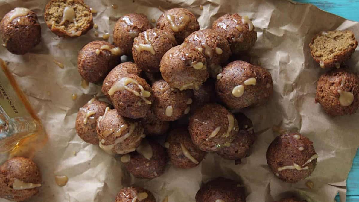 A pile of round, baked brown cookies drizzled with glaze, arranged on crumpled parchment paper with a few cookies partially broken open.