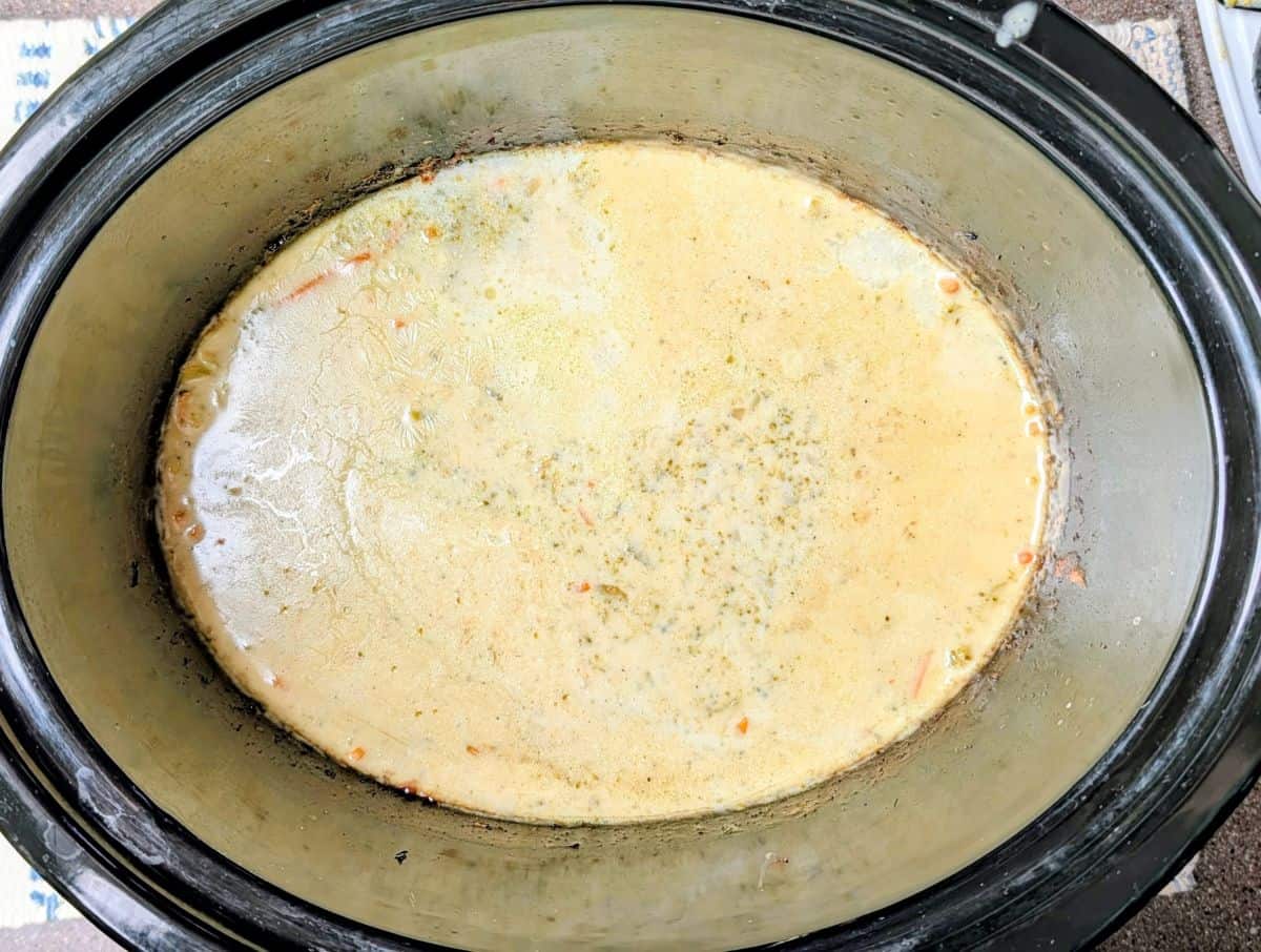 A creamy soup with visible herbs and small vegetable pieces inside a black slow cooker.