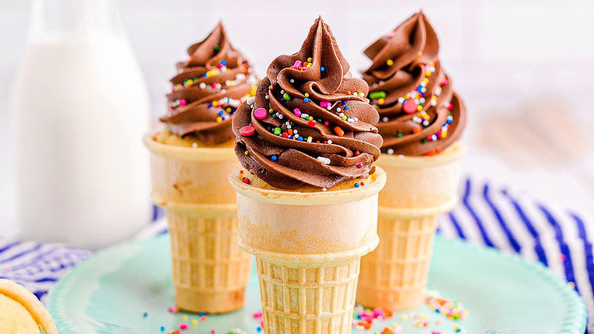 Three ice cream cones filled with chocolate soft-serve topped with rainbow sprinkles, placed on a light blue plate.