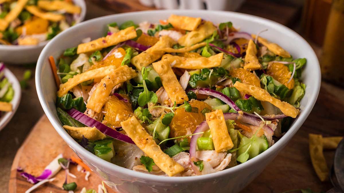 A bowl of salad with sliced red onions, orange segments, greens, and crispy wonton strips.