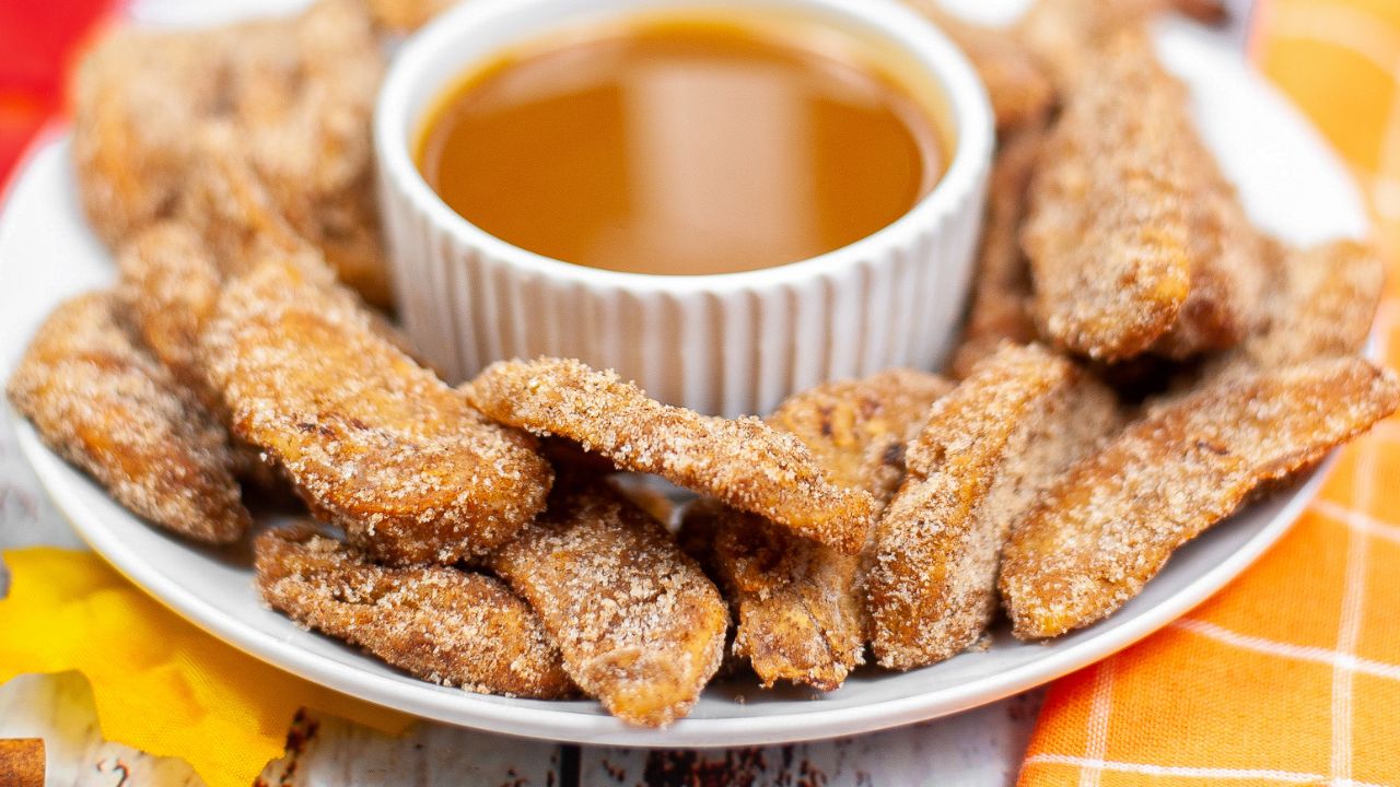 A plate of sugar-coated fried strips arranged around a white ramekin filled with caramel dipping sauce.