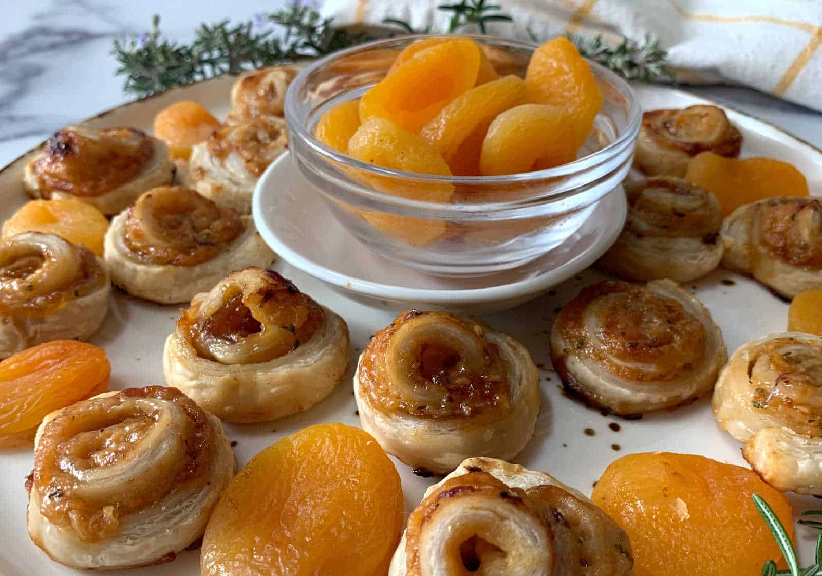 A plate of pastry pinwheels and dried apricots arranged around a small glass bowl filled with more dried apricots.