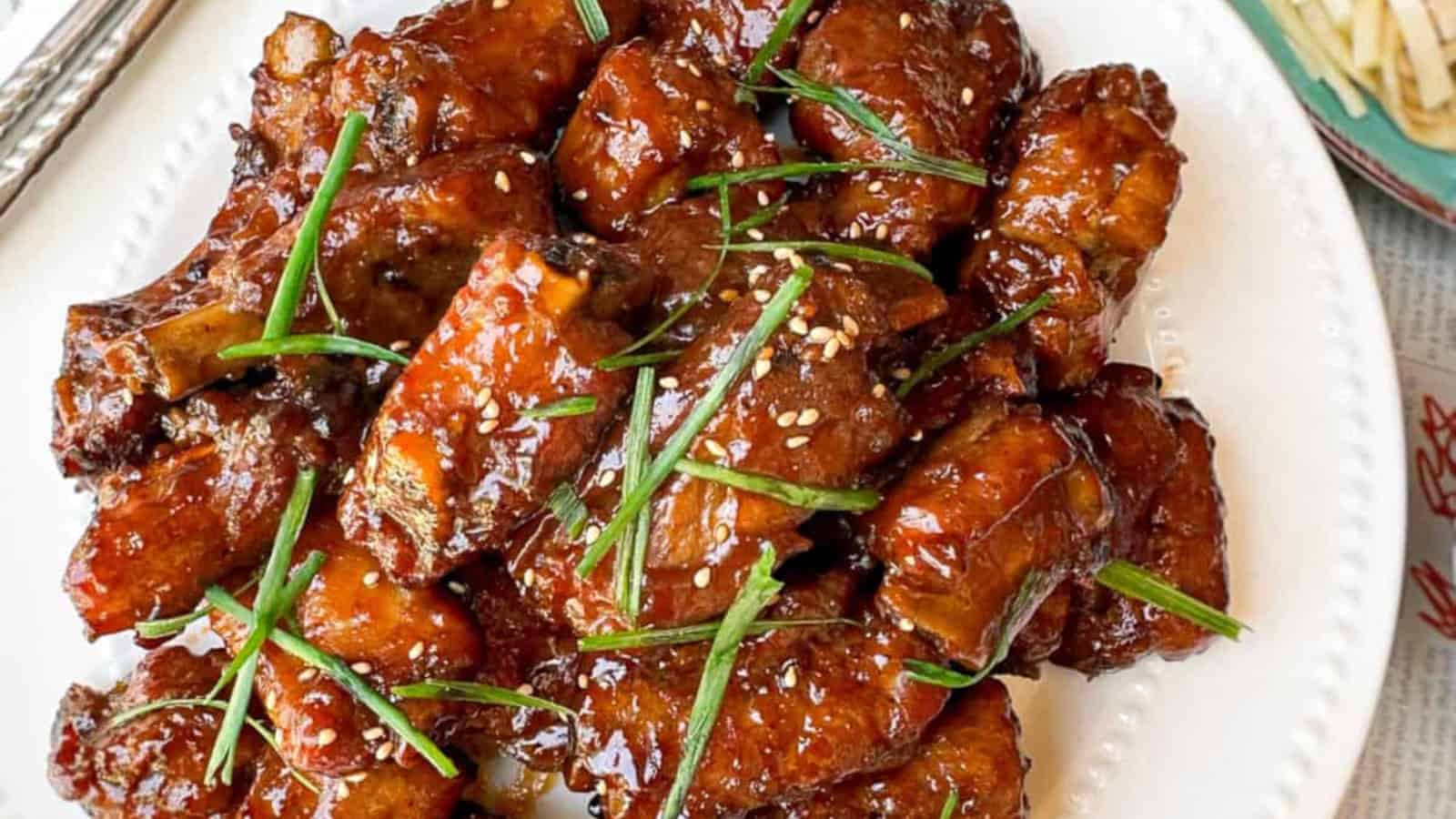 A plate of glazed pork ribs garnished with sesame seeds and chopped green onions.