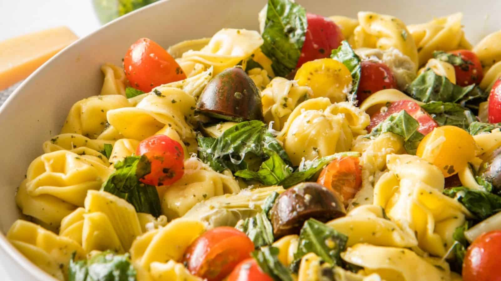 Bowl of tortellini pasta salad with cherry tomatoes, fresh spinach, basil leaves, and grated cheese.