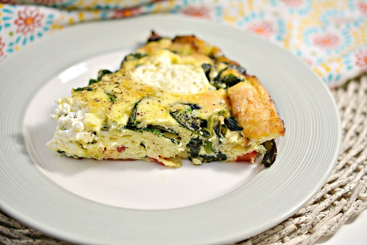A slice of vegetable frittata with spinach and cheese served on a white plate.