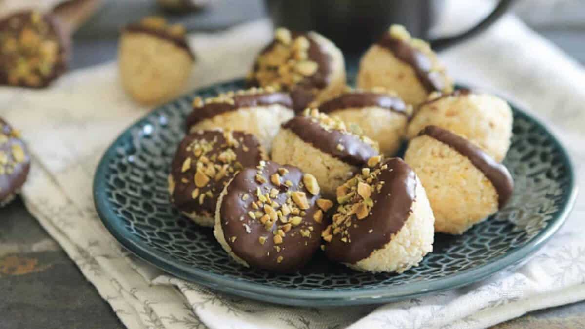 A blue patterned plate with round cookies partially dipped in chocolate and sprinkled with chopped nuts, arranged on a folded cloth.