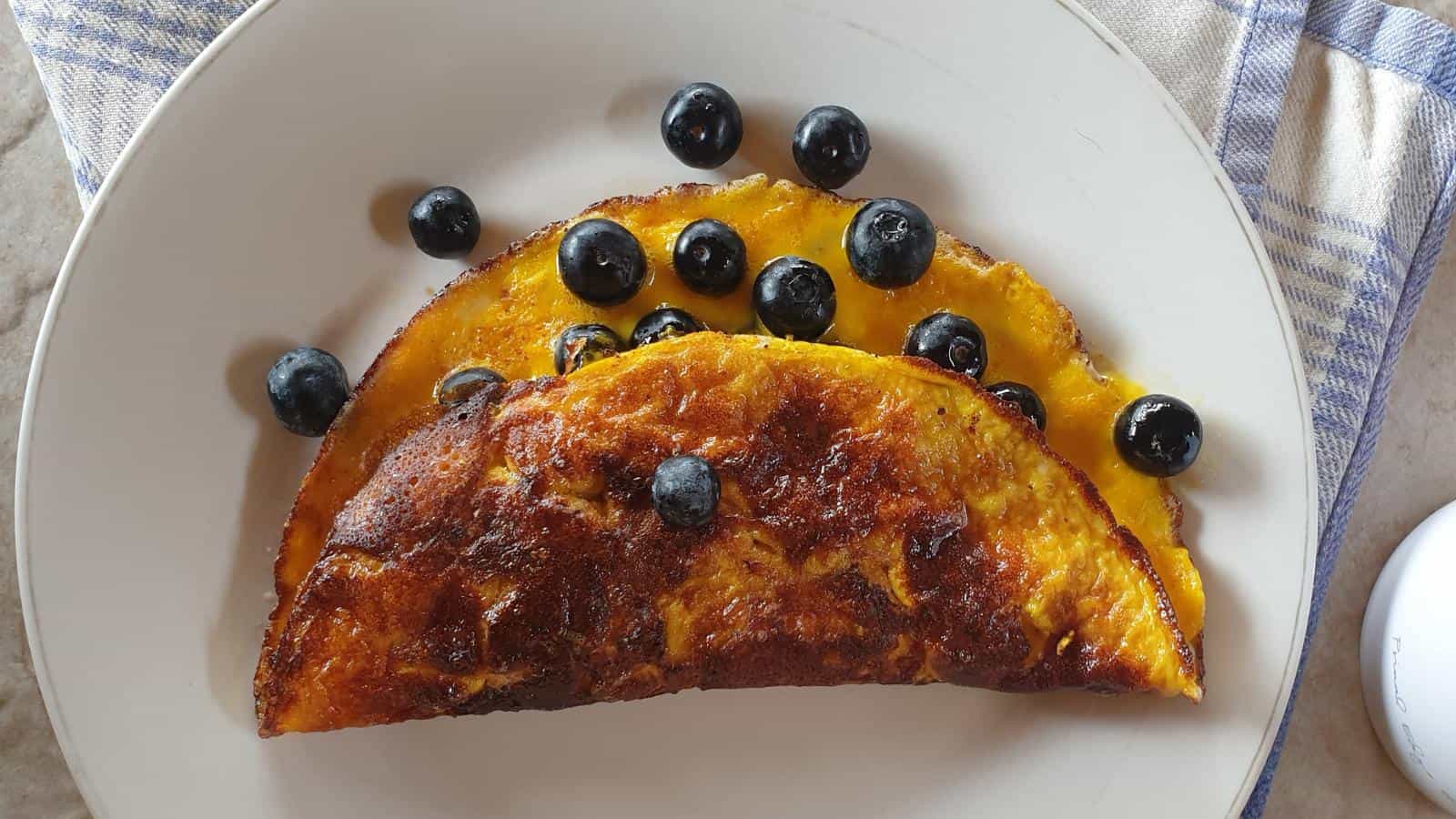 A folded omelette with melted cheese is garnished with fresh blueberries on a white plate.