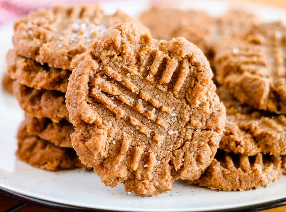 A stack of peanut butter cookies with crisscross fork marks on top, sprinkled with coarse salt, displayed on a white plate.