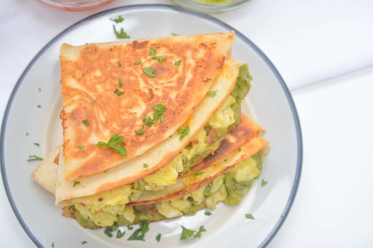 A plate with folded quesadillas filled with scrambled eggs and avocado, garnished with chopped herbs.