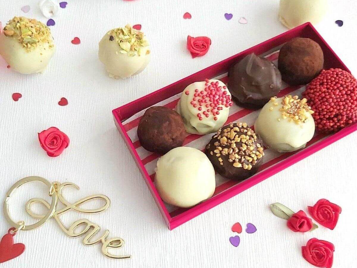 A box of assorted chocolate truffles is displayed on a white surface decorated with small red roses and a gold keychain that says Love.