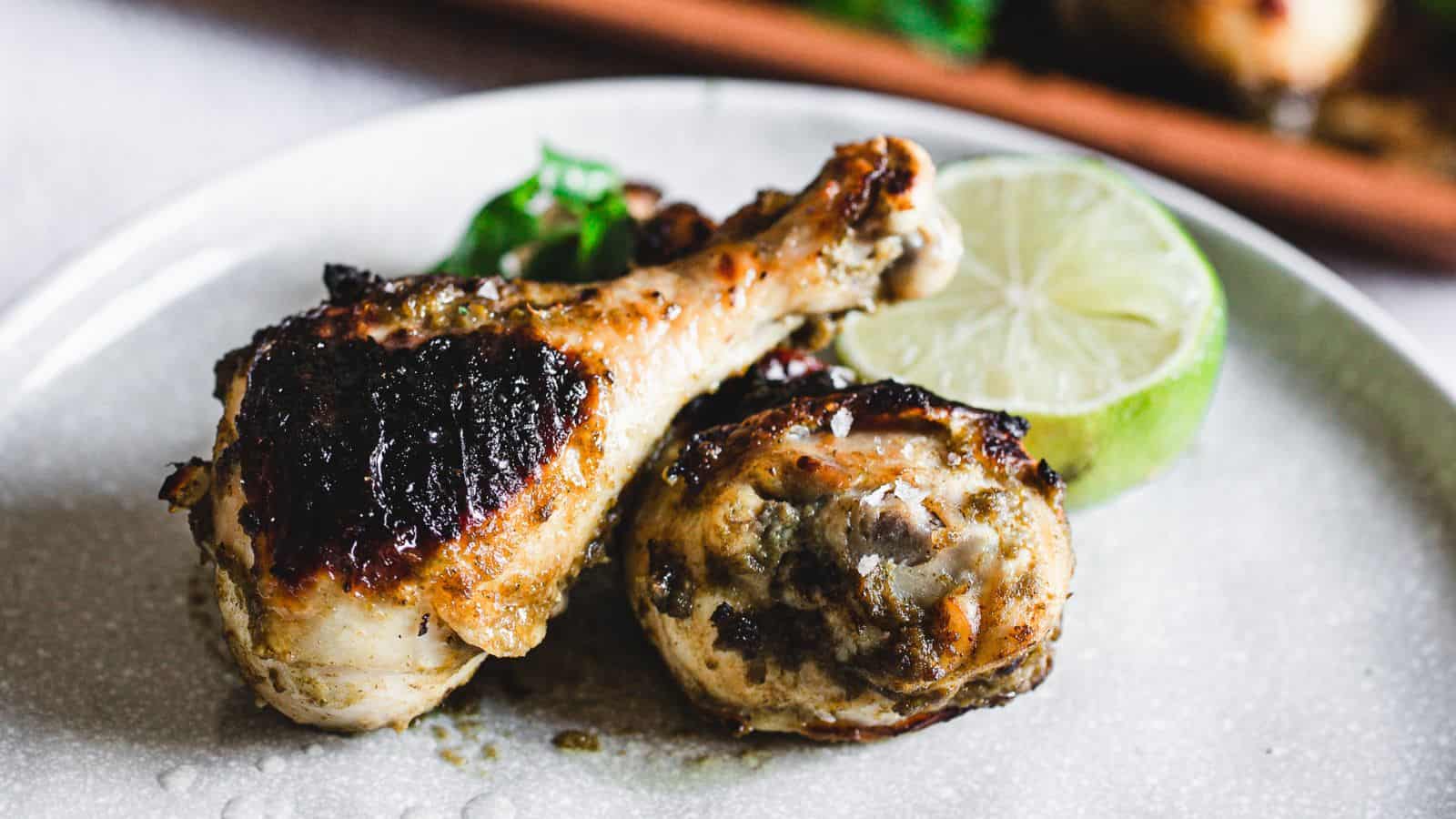 Two pieces of grilled chicken with char marks served on a plate with a wedge of lime and a garnish.