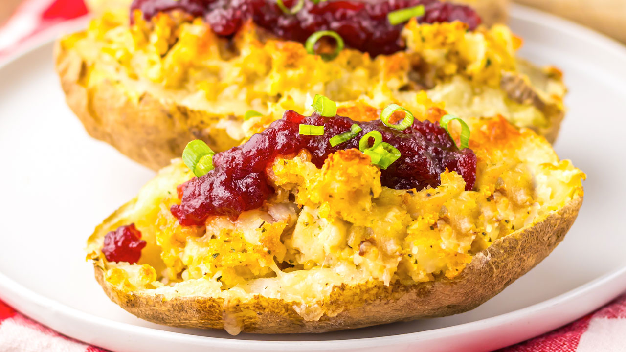 Twice-baked potato halves topped with a red sauce and chopped green onions, served on a white plate.