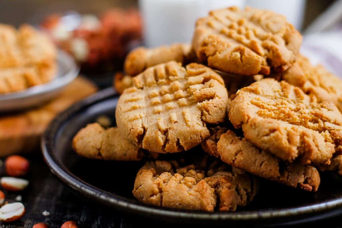 A plate of homemade peanut butter cookies stacked on top of each other, with a crisscross fork pattern on top of each cookie.