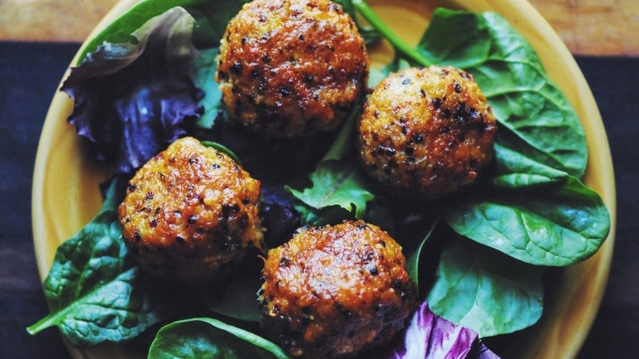 Four baked meatballs are served on a bed of fresh mixed greens on a yellow plate.