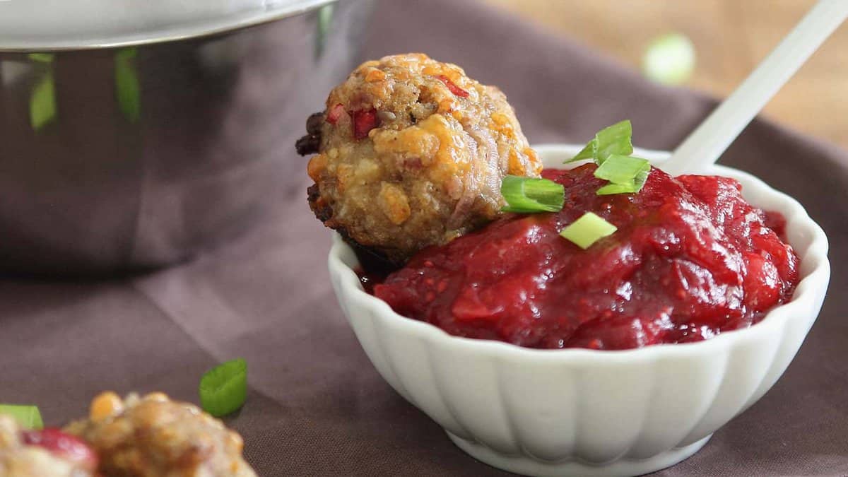 A small white bowl filled with red cranberry sauce, topped with a meatball and garnished with chopped green onions.