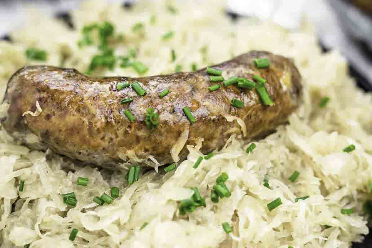 A cooked sausage rests on a bed of sauerkraut, garnished with chopped chives.