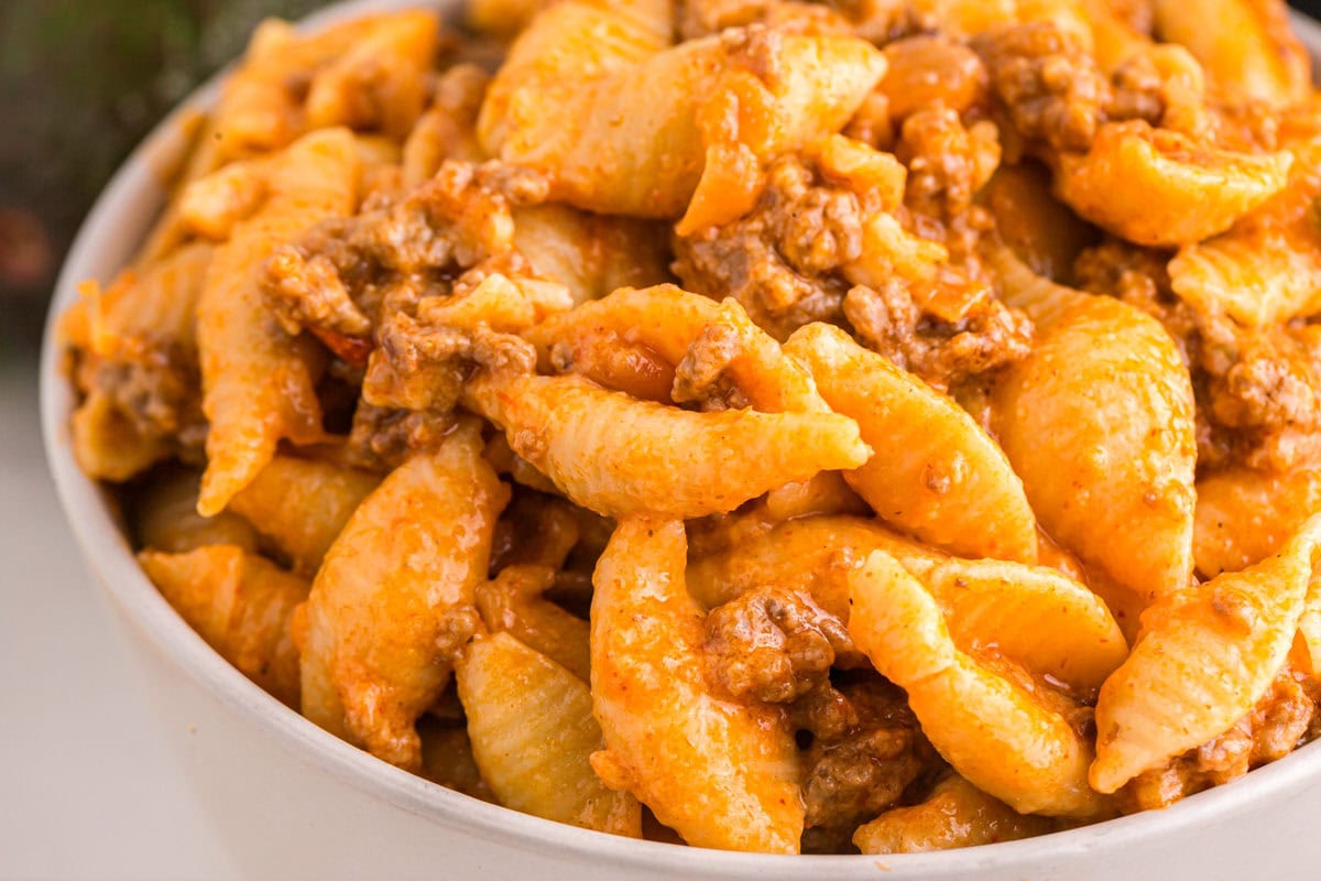 A bowl filled with pasta shells mixed with ground beef and a creamy, orange-colored sauce.