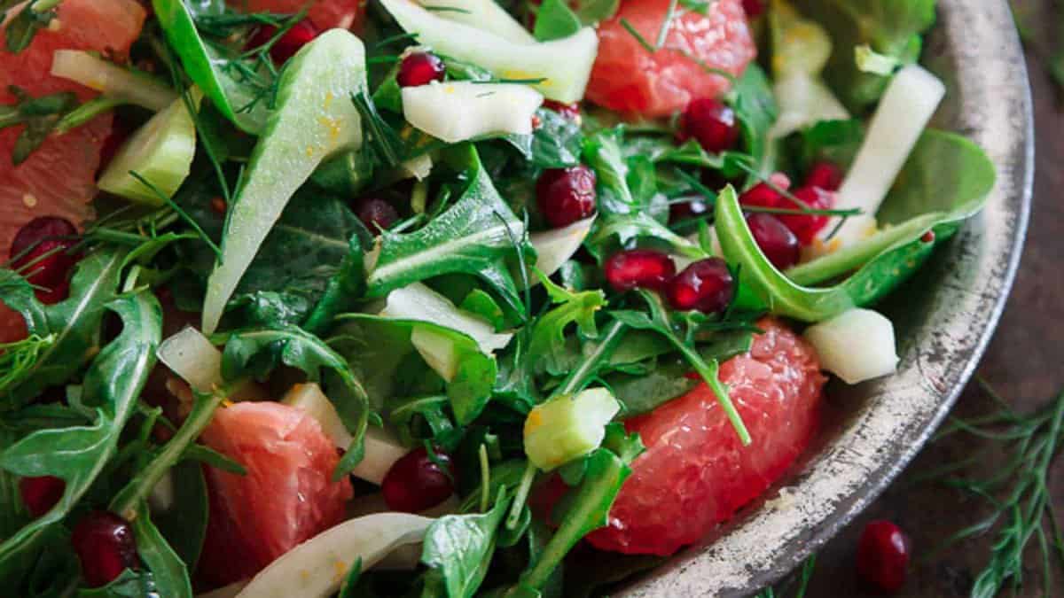 A salad with arugula, grapefruit segments, fennel slices, pomegranate seeds, and fresh herbs in a bowl.