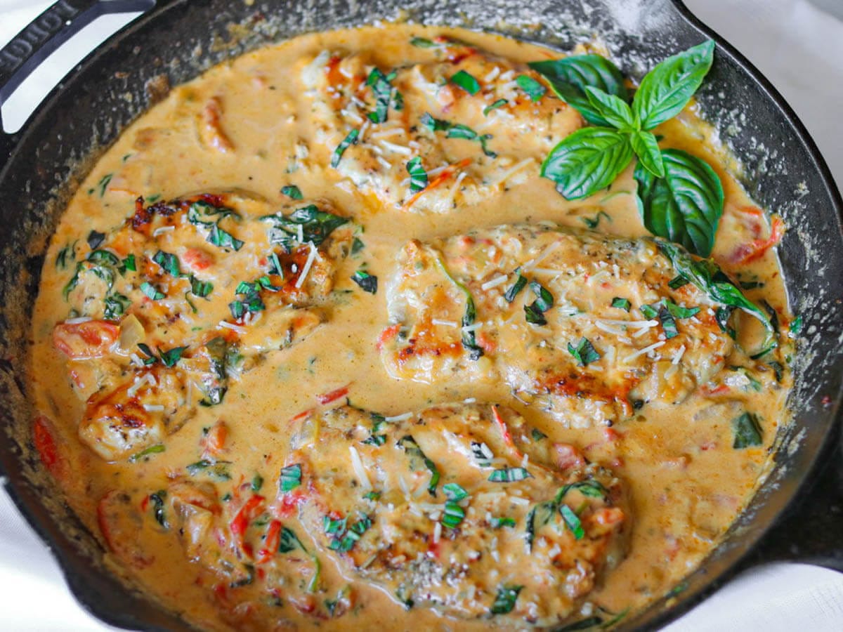 Chicken breasts in a creamy tomato and spinach sauce, garnished with basil leaves and grated cheese, served in a black skillet.