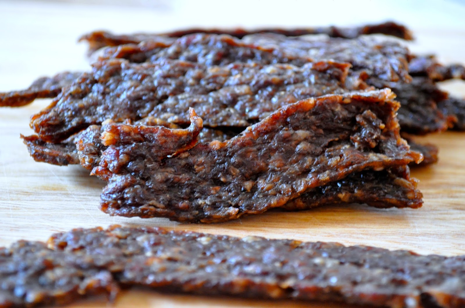 Several pieces of beef jerky are stacked on a wooden surface.