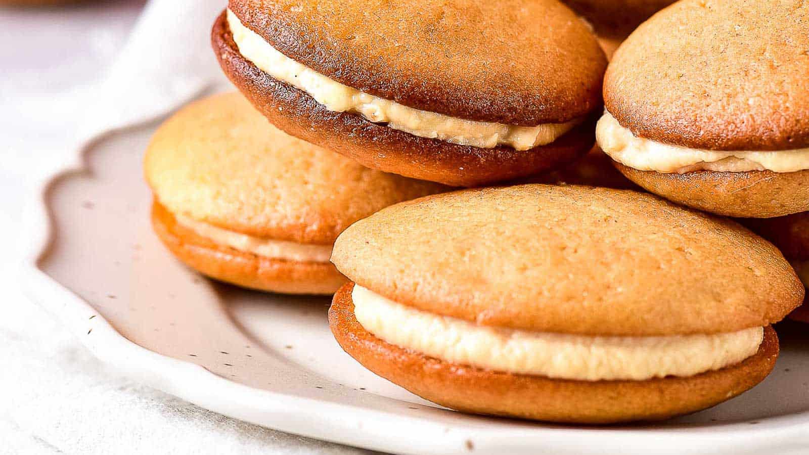 A plate of whoopie pies with golden brown cake-like cookies and creamy filling inside.