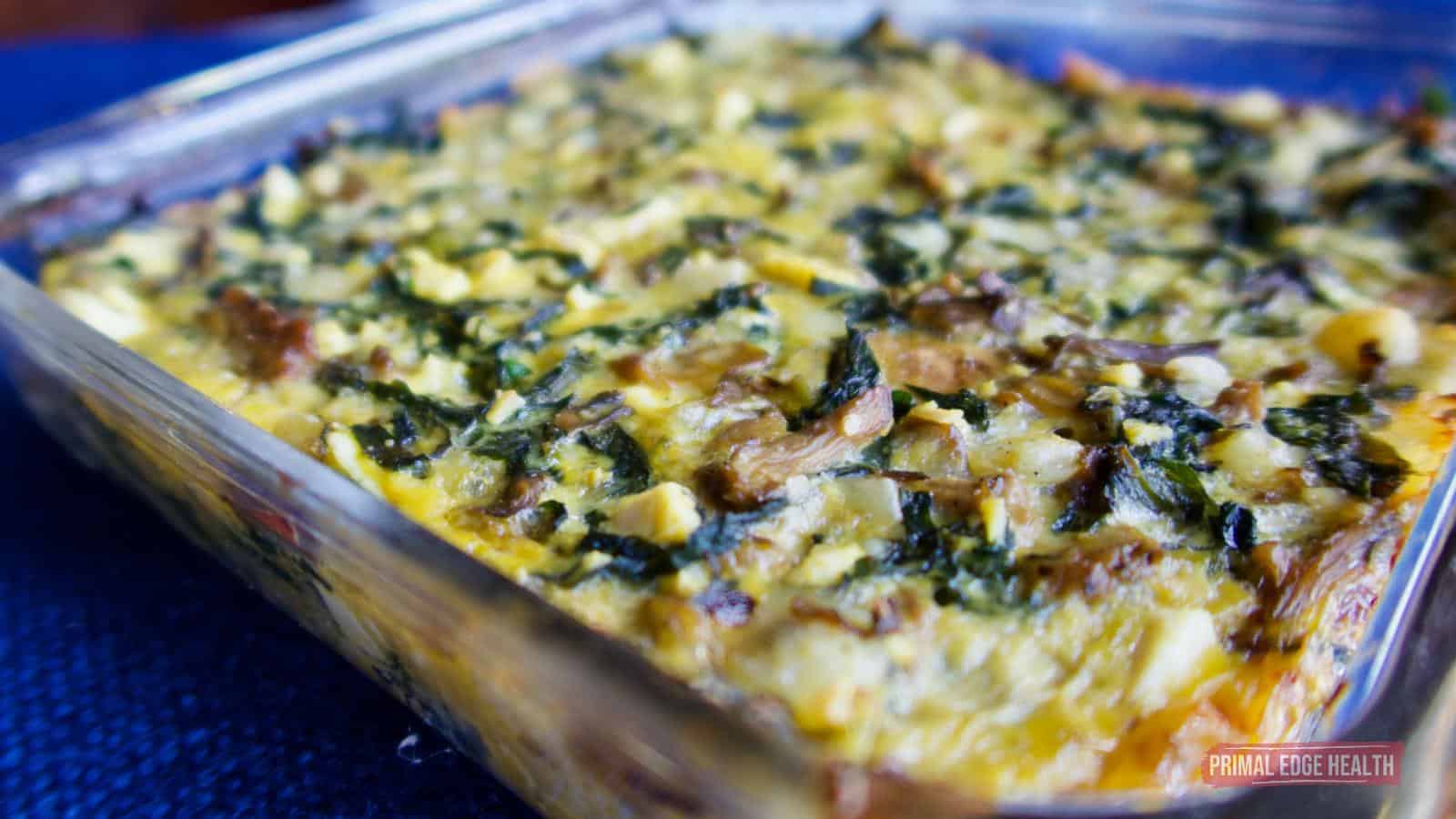 A close-up of a baked egg casserole in a glass dish, featuring visible greens and cheese on top.