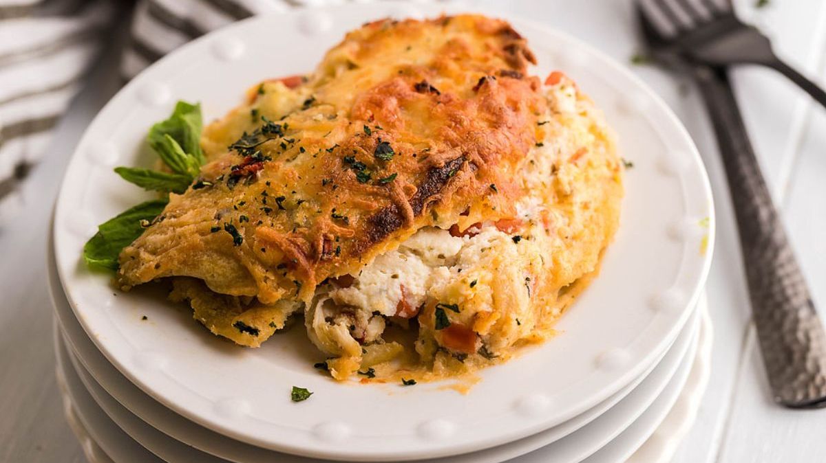 A serving of cheesy baked lasagna with visible layers of pasta, ricotta, and tomato sauce on a white plate, garnished with herbs.